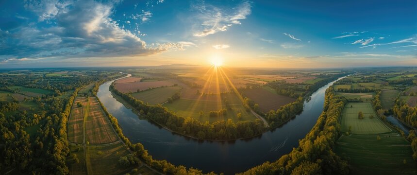 Wide aerial panorama of river bordered by farmland and rolling hills with godrays