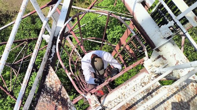 Man climbing vertical cage ladder inside 75m repurposed radar tower