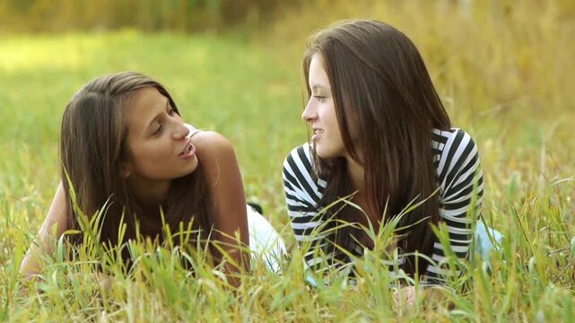 Two cheerful girls teenagers lie on grass