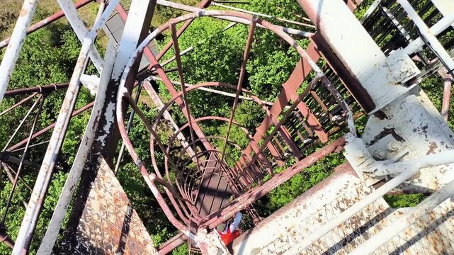 Man climbing vertical cage ladder inside 75m repurposed radar tower