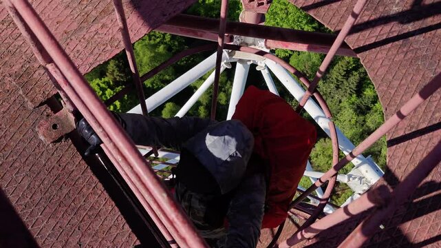 Man climbing vertical cage ladder inside 75m repurposed radar tower
