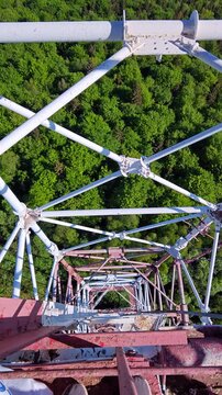 High angle POV looking down through steel lattice tower onto green forest