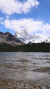 View of Mount Fitz Roy rising above the calm waters of Laguna Capri with snow-capped peaks and a blue sky in Fitz Roy, Santa Cruz Province, Argentina.