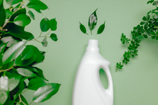 Mockup bottle laundry detergent or fabric softener close up with green plant leaves on green background top view. Natural washing and cleaning product for home.