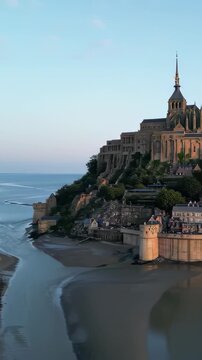 Bastille Day aerial Mont Saint-Michel island abbey, tidal flats, golden archangel spire, morning light, cinematic drone orbit, France July 14 national day landmark b-roll