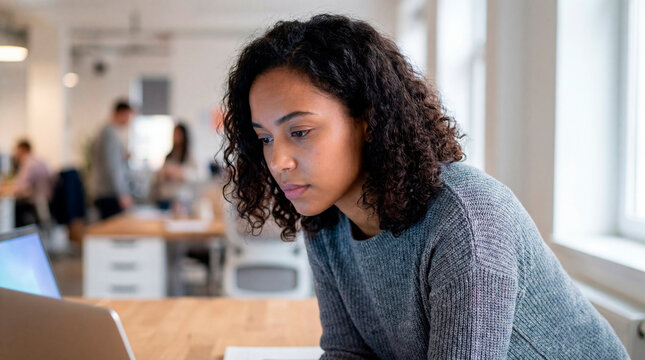 Focused young multiracial woman working on laptop computer in bright modern office