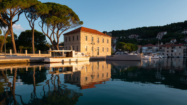 Historic stone house in Jelsa harbor reflecting in water at sunrise