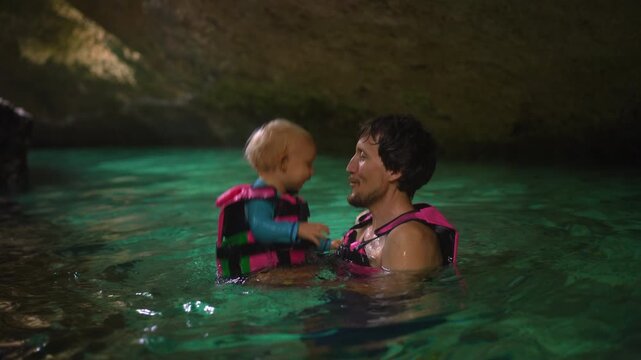 Father holding toddler son in blue cenote cave water.
