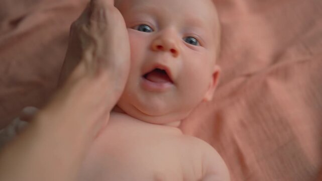 Father hand stroking baby on orange cloth with hiccups.