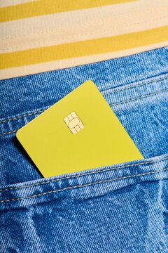 Closeup of a yellow debit card with a microchip sticking out of the back pocket of a pair of jeans.