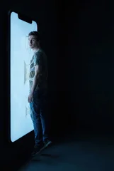 Conceptual Metaphor of a Young Man Consumed and Addicted to a Glowing Smartphone Screen © IBEX.Media