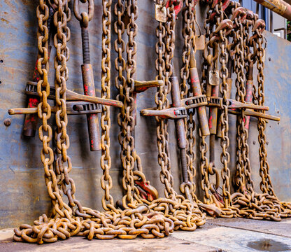 Close view of metal chains hanging against wooden surface in a workshop setting during daytime with natural light