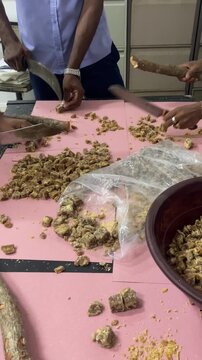 close up of traditional sweet jaggery being cut into pieces by hand, authentic food preparation, rustic texture, cultural dessert processing