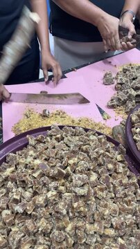 close up of traditional sweet jaggery being cut into pieces by hand, authentic food preparation, rustic texture, cultural dessert processing
