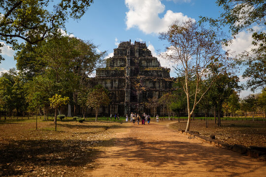 View of the ancient Prasat Thom pyramid temple at the Koh Ker archaeological site, with lush trees and visitors walking on a dirt path in Siem Reap, Siem Reap Province, Cambodia.