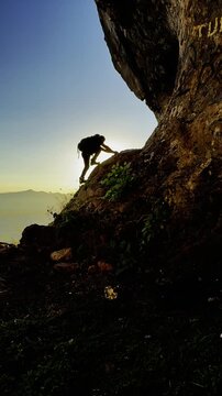 Silhouette of a man climbing a cave and cliff to sit and watch the sunrise
