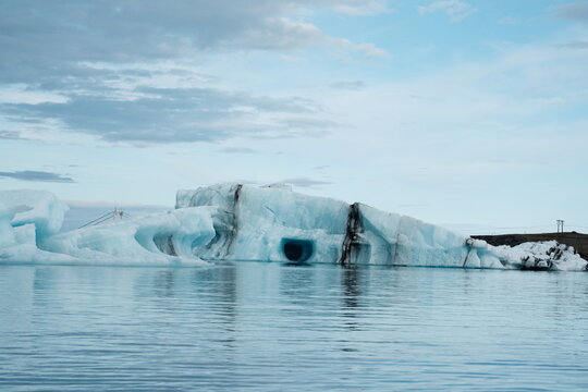View of Jokulsarlon Glacier Lagoon with floating blue icebergs and calm water under a cloudy sky in Sveitarfelagid Hornaf, Iceland.