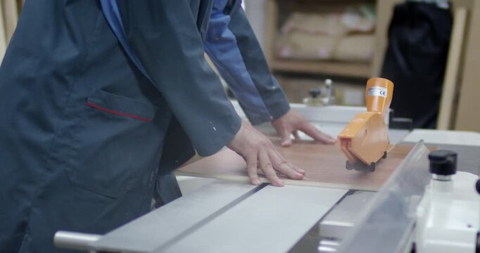 Mid section of woodworker using sliding table saw machine with orange blade guard to cut wooden panel