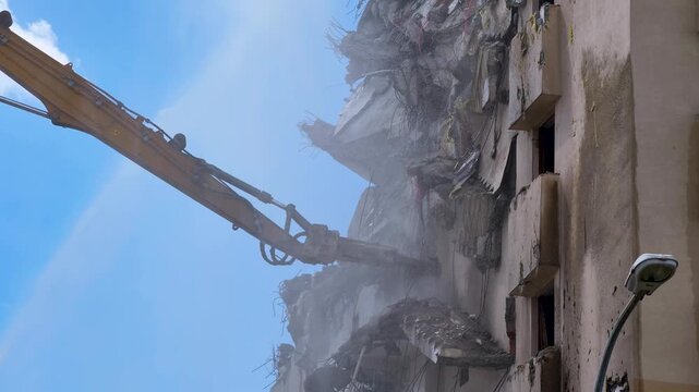 Building demolition takes place with heavy machinery in downtown area under blue sky during daytime