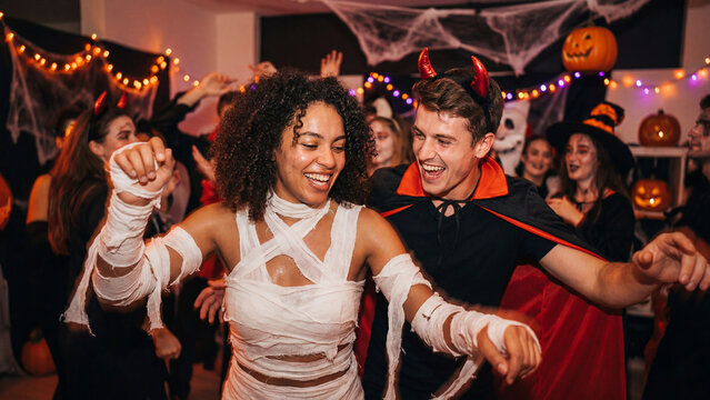 Halloween party dancing celebration with young diverse couple in mummy demon costumes having fun for social dating entertainment website promotional content