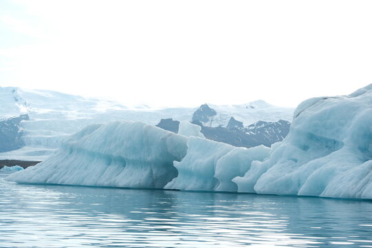 View of Jokulsarlon Glacier Lagoon with massive blue icebergs floating in calm water against a backdrop of snow-covered mountains in Sveitarfelagid Hornaf, Iceland.