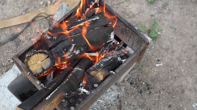 High angle 4K footage of a small metal grill with burning wood logs