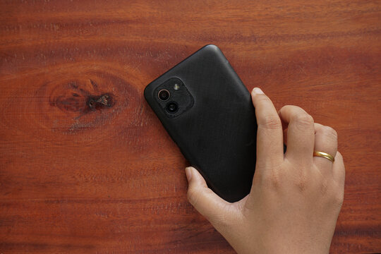 Hand holding a smartphone face down on a wooden table. Top view with a clean, minimalist composition for technology, communication, or digital wellbeing concept