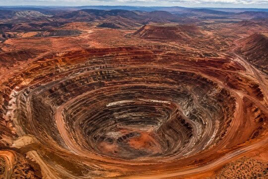 An aerial view of a vast open-pit mine with terraced reddish-brown soil.