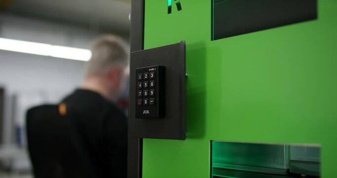Electronic keypad lock mounted on a green secure locker cabinet in a bright warehouse facility