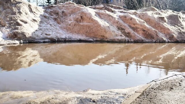 Dirty melting snow creating a large puddle with reflections of the early spring sky
