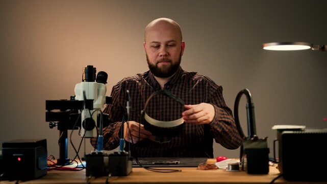 Repair technician inspecting small electronics at a cluttered workbench with microscope