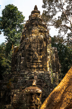 View of the iconic stone face tower at Bayon Temple, surrounded by lush jungle trees and ancient weathered masonry in Krong Siem Reap, Siem Reap Province, Cambodia.