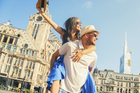 Beautiful young tourist couple having fun piggyback visiting Batumi Georgia. Tourists enjoying holiday in Europe in famous landmark - Vacation and happy lifestyle concept. Caucasus travel destination