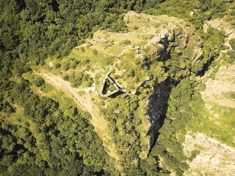 Aerial top down view of Armazi Fortress ruins on steep ridge with tilted rock formations and forested hills, part of important ancient defense system near Mtskheta, Georgia