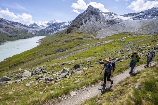 Three mountaineers on a hiking trail at a blue mountain lake, reservoir Lac des Dix, behind mountain peak Mont Blanc de Cheilon, H&eacute;rm&eacute;nence, Valais Alps, Valais, Switzerland