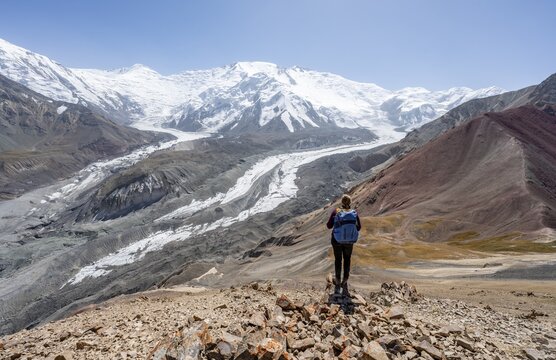 Mountaineer at Traveller's Pass with view of impressive mountain landscape, high mountain landscape with glacier moraines and glacier tongues, glaciated and snow-covered mountain peaks, Lenin Peak and Peak of the XIX Party Congress of the CPSU, Trans Alay Mountains, Pamir Mountains, Osh Province, Kyrgyzstan
