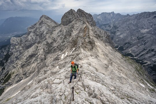 Mountaineer with helmet climbing in a secured climb on the rock, on a narrow rocky ridge, crossing the Jubil&auml;umsgrat, view of Rheintal and Alpspitze, Wetterstein range, Bavaria, Germany