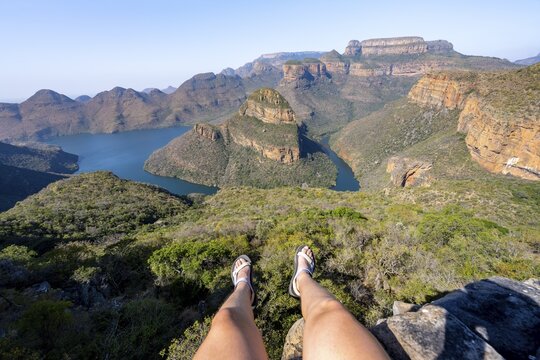 Legs of a sitting woman, view of river bend at Blyde River Canyon with Three Rondawels peak, view of canyon with Blyde River and table mountains in the evening light, canyon landscape, Panorama Route, Mpumalanga, South Africa