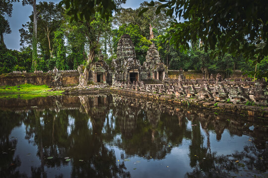 View of the ancient stone ruins of Preah Khan temple surrounded by lush jungle trees and a reflective moat with stone statues in Krong Siem Reap, Siem Reap Province, Cambodia.
