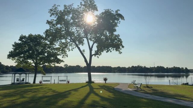 Sun setting behind trees over lake with gazebo and park landscape