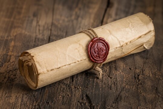 A rolled antique parchment scroll sealed with red wax featuring a fleur-de-lis on a wooden surface.