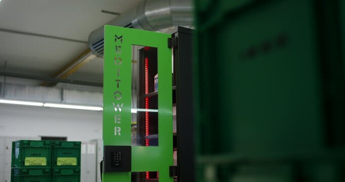 Green vertical automated storage system tower standing in a spacious industrial warehouse hall