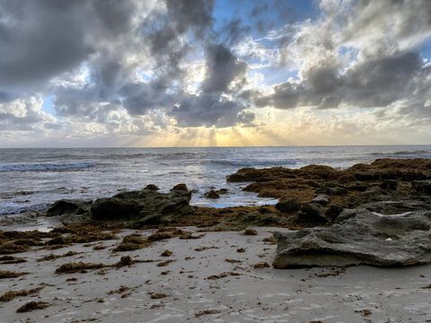 View of Cottesloe Beach at sunset with sun rays breaking through dramatic clouds over the rocky shoreline and sandy beach in Western Australia, Australia.