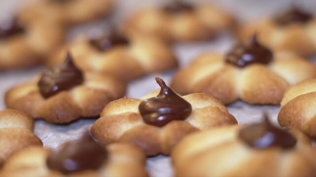 Close-up view of freshly baked cookies with chocolate topping, arranged neatly on a baking sheet, showcasing the texture and details of the cookies in a well-lit kitchen environment