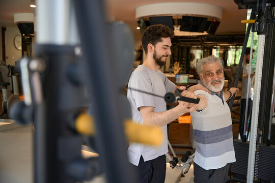 Senior man exercising with assistance in modern gym