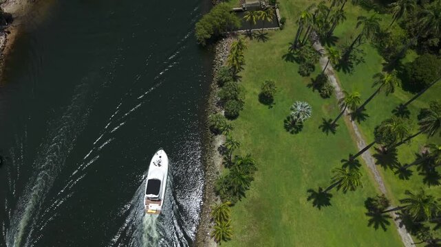Top down aerial view of yachts cruising near a green waterfront park