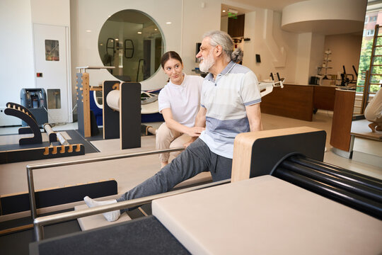 Senior man exercising with support from young woman in rehab center