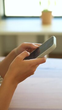 Close-up view of female hands holding a modern smartphone, with fingers tapping and scrolling on the touchscreen while browsing social media, texting, or shopping online in a bright room
