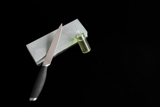Knife rests on whetstone. Oil bottle nearby, ready for sharpening. Clean background, professional look. Perfect for kitchen, cooking, or tool imagery. Sharpness and care emphasized in this still image