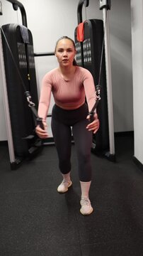 Vertical screen Young woman performs standing cable fly exercise focusing on controlled movement chest activation and upper body strength during an independent gym workout